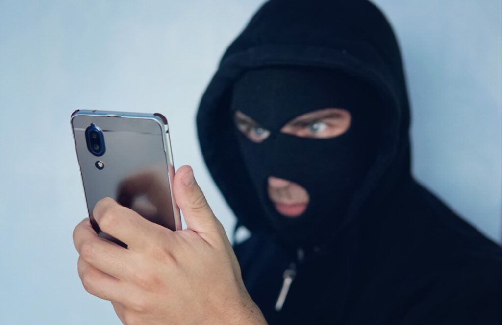 homem encapuzado olhando fixamente para um celular com cara de mau, representando golpes de engenharia social