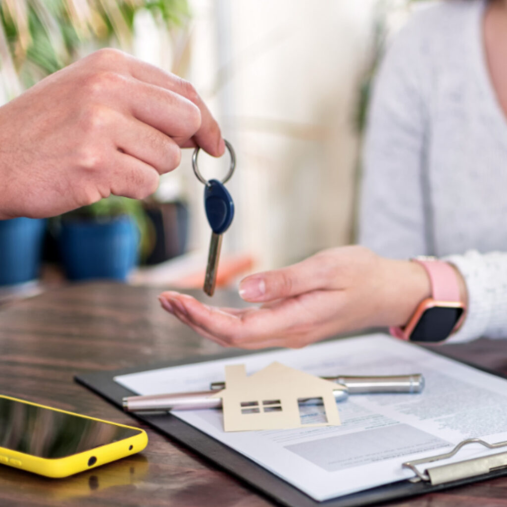 uma pessoa entregando uma chave para outra pessoa, de baixo de suas mãos um contrato, representando golpes imobiliários