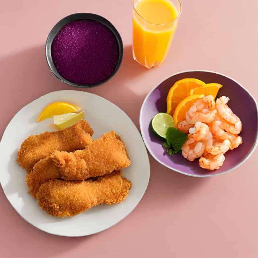 um prato com peixes fritos empanados, uma tigela com camarões e limão, uma tigela de açaí e um copo de suco de laranja