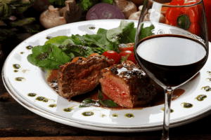 carne vermelha em um prato e uma taça de vinho