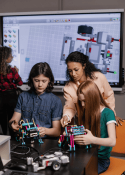 uma professora em uma sala de aula ensinando robotica para duas crianças